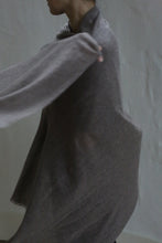 Load image into Gallery viewer, A person wears the Tissue Weight Cashmere Scarf in taupe, loosely draped with one arm extended, partially obscured against a plain light background. Their face is mostly out of frame.