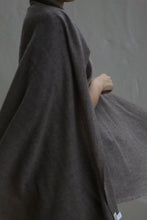Load image into Gallery viewer, A person wears the Tissue Weight Cashmere Scarf in taupe, draped softly around their shoulders against a plain gray background, standing partially turned with one arm bent. Their face is mostly out of frame.