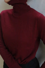 Load image into Gallery viewer, A person wearing the Cashmere Turtleneck | Wine, shown from shoulders to waist with black pants and their face partially out of frame. This 100% cashmere sweater is hand washable for easy care.