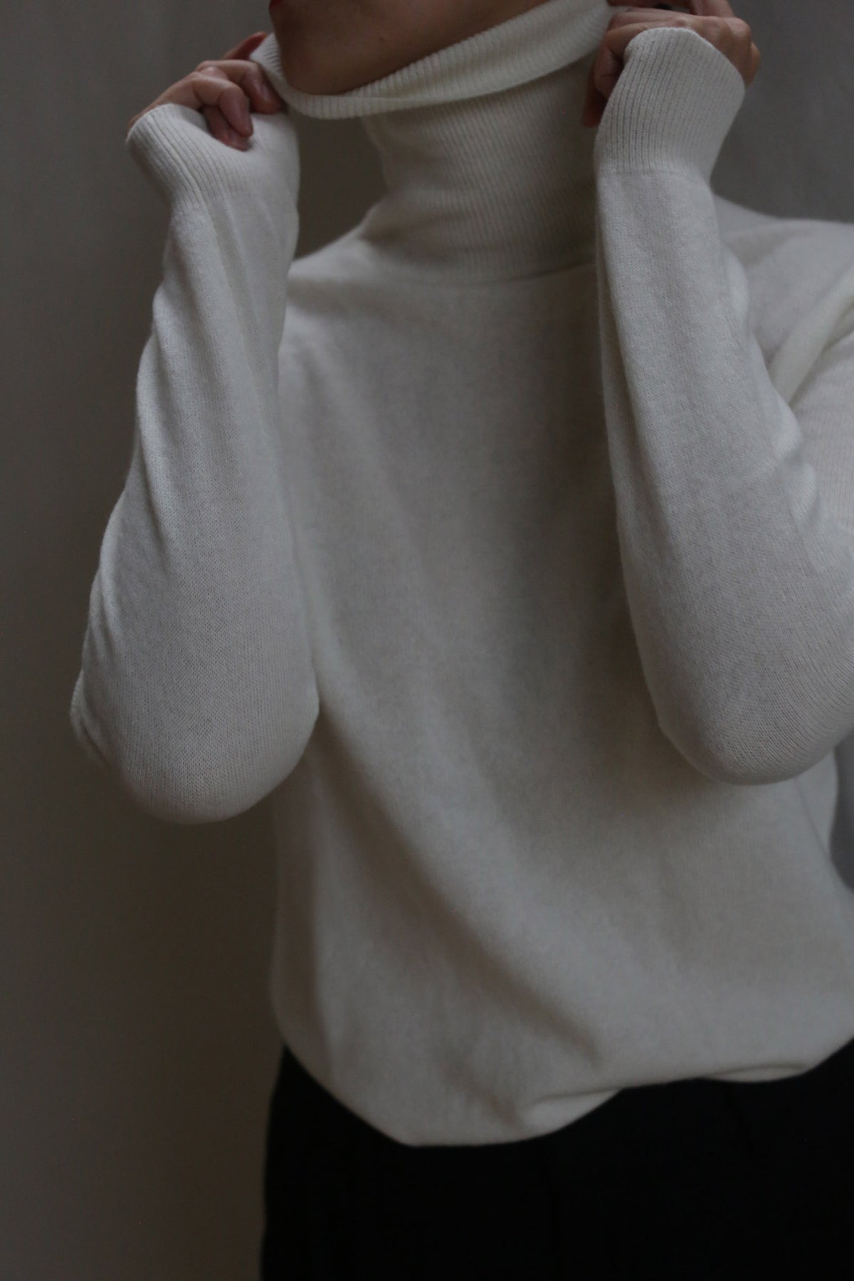 Wearing the Cashmere Turtleneck | Ivory, a person pulls up the collar to partially cover their face. The image, cropped to highlight only the head, neck, and upper torso, features a neutral backdrop.