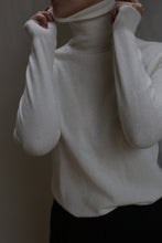 Load image into Gallery viewer, Wearing the Cashmere Turtleneck | Ivory, a person pulls up the collar to partially cover their face. The image, cropped to highlight only the head, neck, and upper torso, features a neutral backdrop.