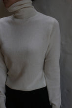 Load image into Gallery viewer, A person models the Ivory Cashmere Turtleneck against a neutral background, paired with dark pants. Their face is partially out of frame and mostly in shadow.