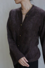 Load image into Gallery viewer, A person wearing the Brushed Cashmere Cardigan in Mink with brass buttons and a gold necklace stands against a plain background, their head turned to the side.