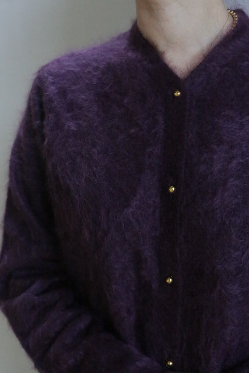 A person is shown from neck to waist wearing the Brushed Cashmere Cardigan in Aubergine, featuring gold buttons. The background is plain and the face is not visible, highlighting this luxury knitwear piece.