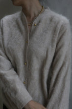 Load image into Gallery viewer, A person wears the Brushed Cashmere Cardigan in Sandstone with brass buttons and a gold beaded necklace, standing against a neutral background. Their face is partially out of frame.