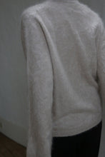 Load image into Gallery viewer, Someone stands with their back to the camera, one arm slightly bent, wearing a soft, light Brushed Cashmere Cardigan in Sandstone with brass buttons. The softly lit background is neutral.