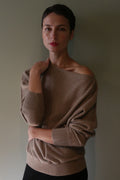 A person wearing a light brown, off-the-shoulder Ballerina’s Cashmere Sweater | Oat with a relaxed silhouette.
