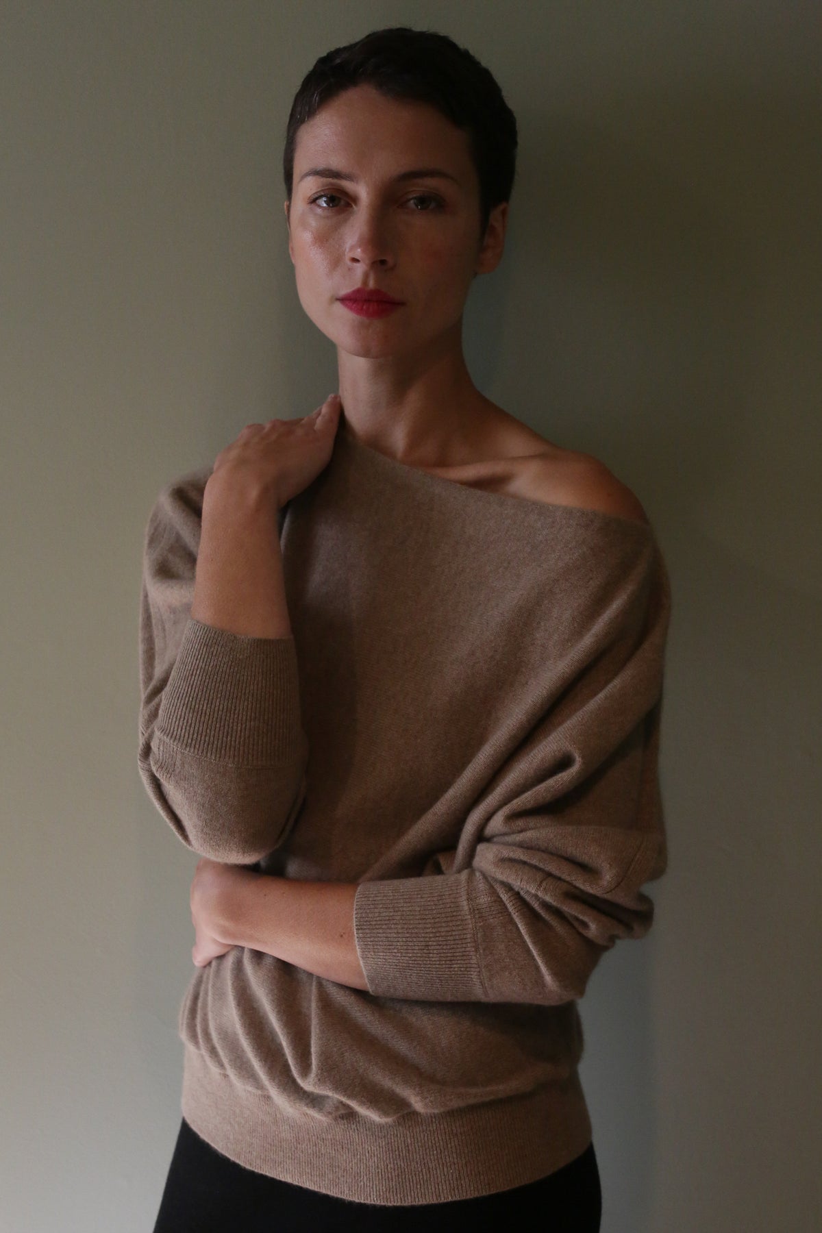 A person wearing a light brown, off-the-shoulder Ballerina’s Cashmere Sweater | Oat with a relaxed silhouette.