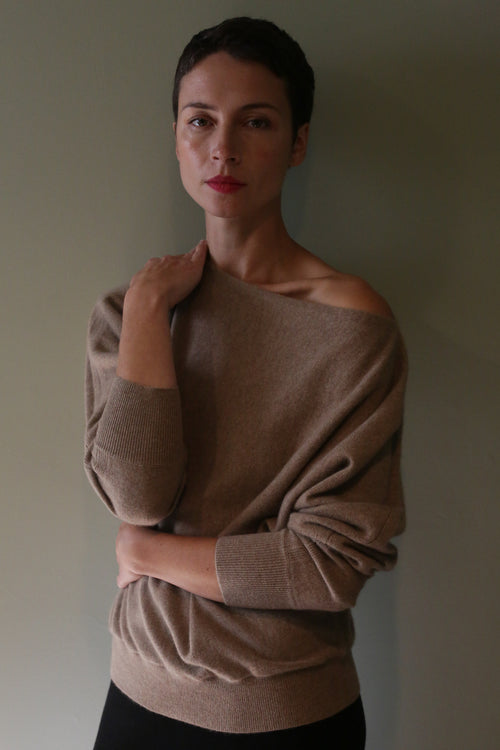 A person wearing a light brown, off-the-shoulder Ballerina’s Cashmere Sweater | Oat with a relaxed silhouette.