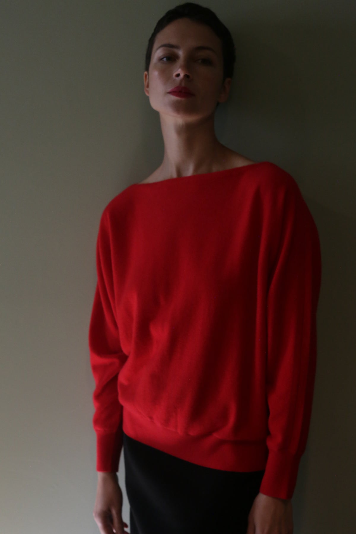 A person wearing a bright red Ballerina’s Cashmere Sweater | Vermillion with a relaxed silhouette and a wide boat neckline.