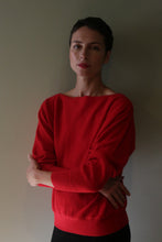 Load image into Gallery viewer, A person with arms crossed wears a vermillion Ballerina’s Cashmere Sweater with a wide boat neckline and a relaxed silhouette.