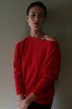 Load image into Gallery viewer, A person wears a relaxed-silhouette Ballerina’s Cashmere Sweater in vermillion with an asymmetrical neckline that drops off one shoulder.