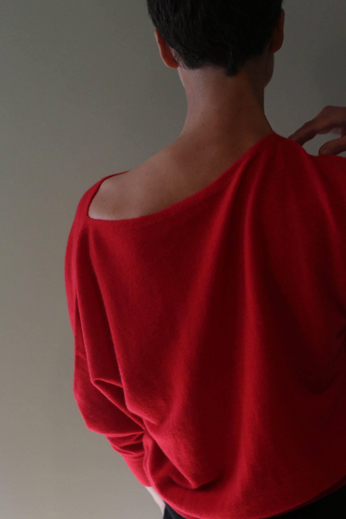 A person viewed from the back wearing a Ballerina’s Cashmere Sweater | Vermillion, featuring a red, relaxed silhouette and a wide, open neckline.