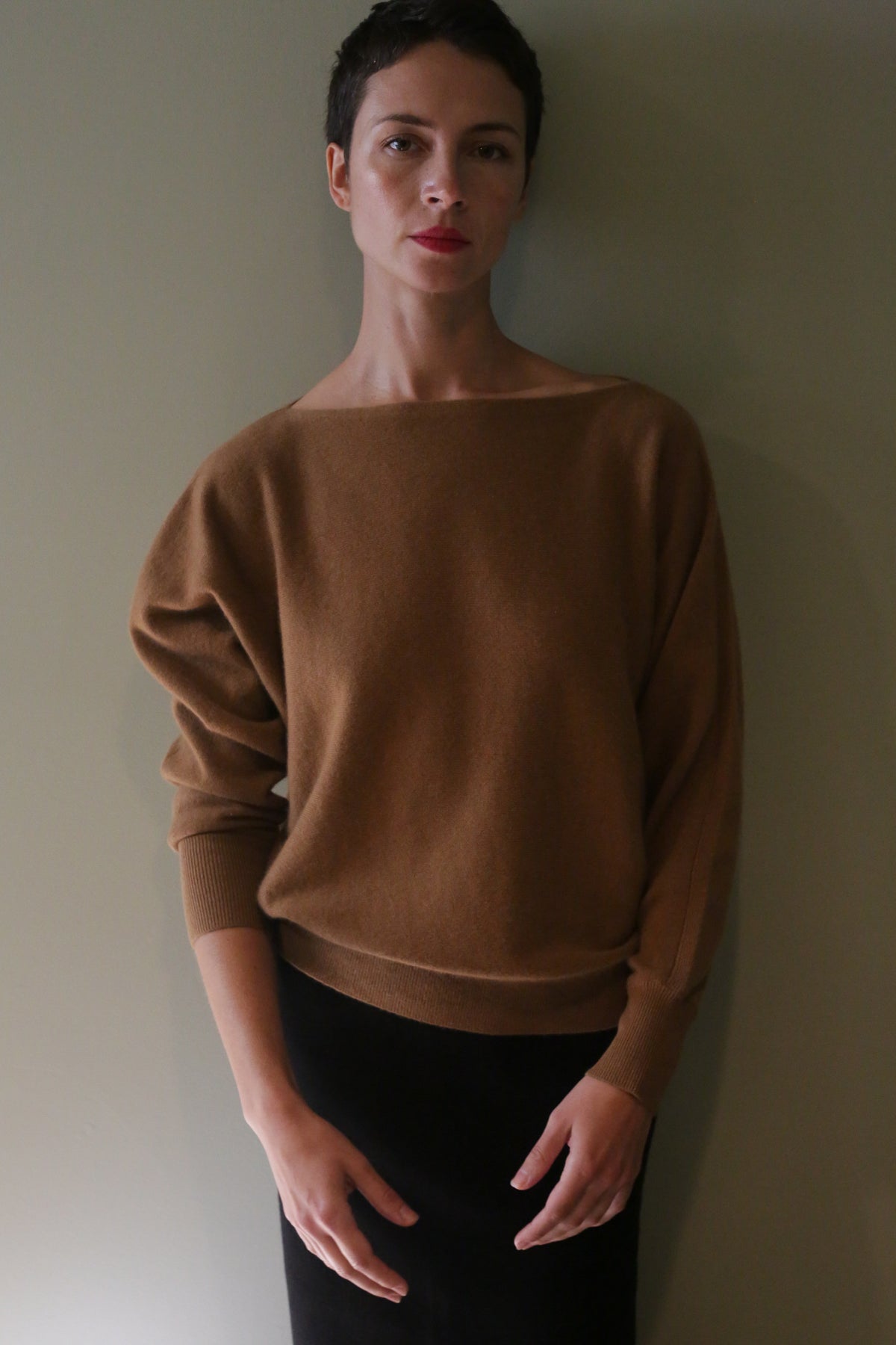 A person wearing a brown, relaxed-fit Ballerina’s Cashmere Sweater | Vicuna with long sleeves and a boat neckline.