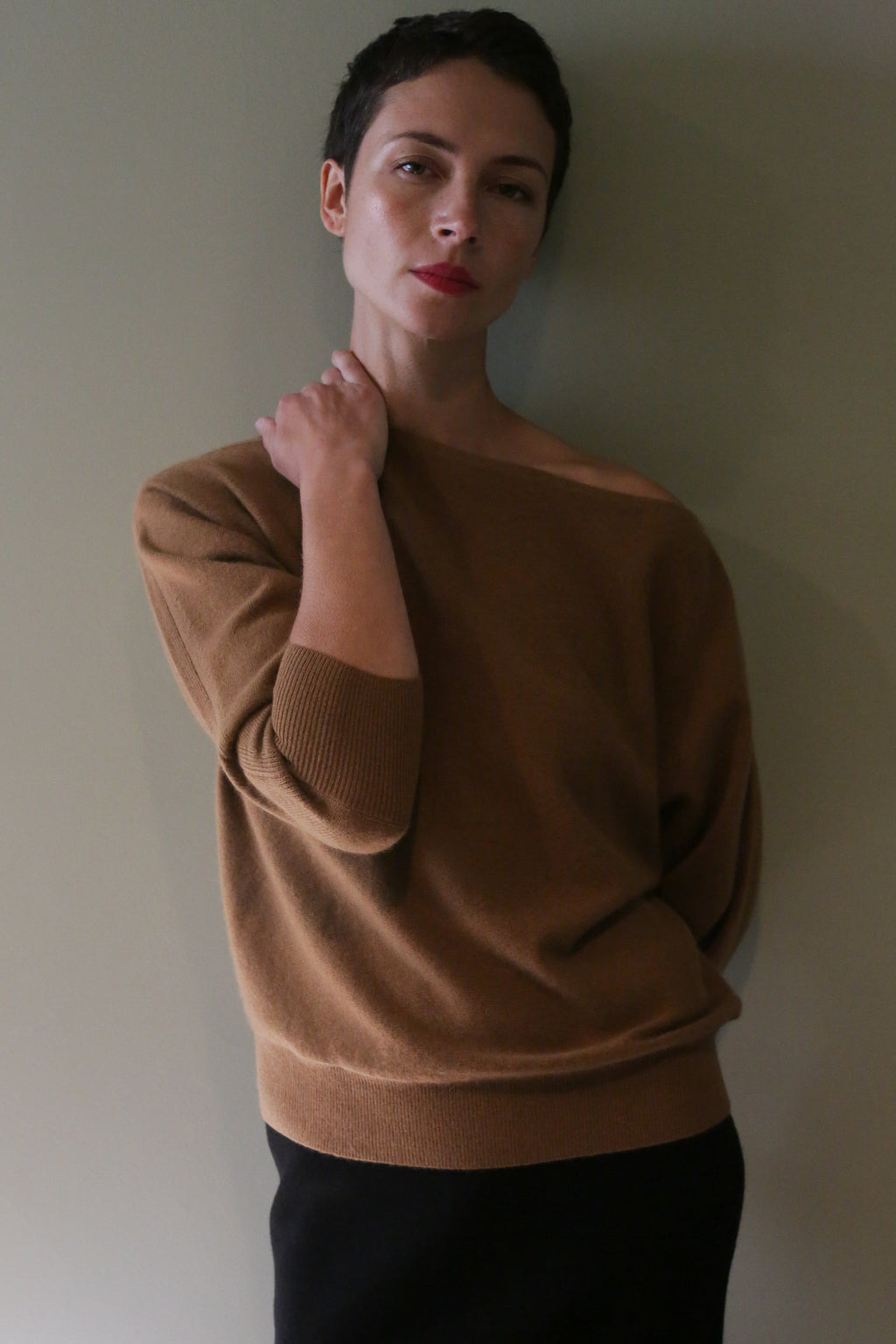 A person wearing a tan, off-the-shoulder Ballerina’s Cashmere Sweater | Vicuna, featuring a relaxed silhouette and three-quarter length sleeves.