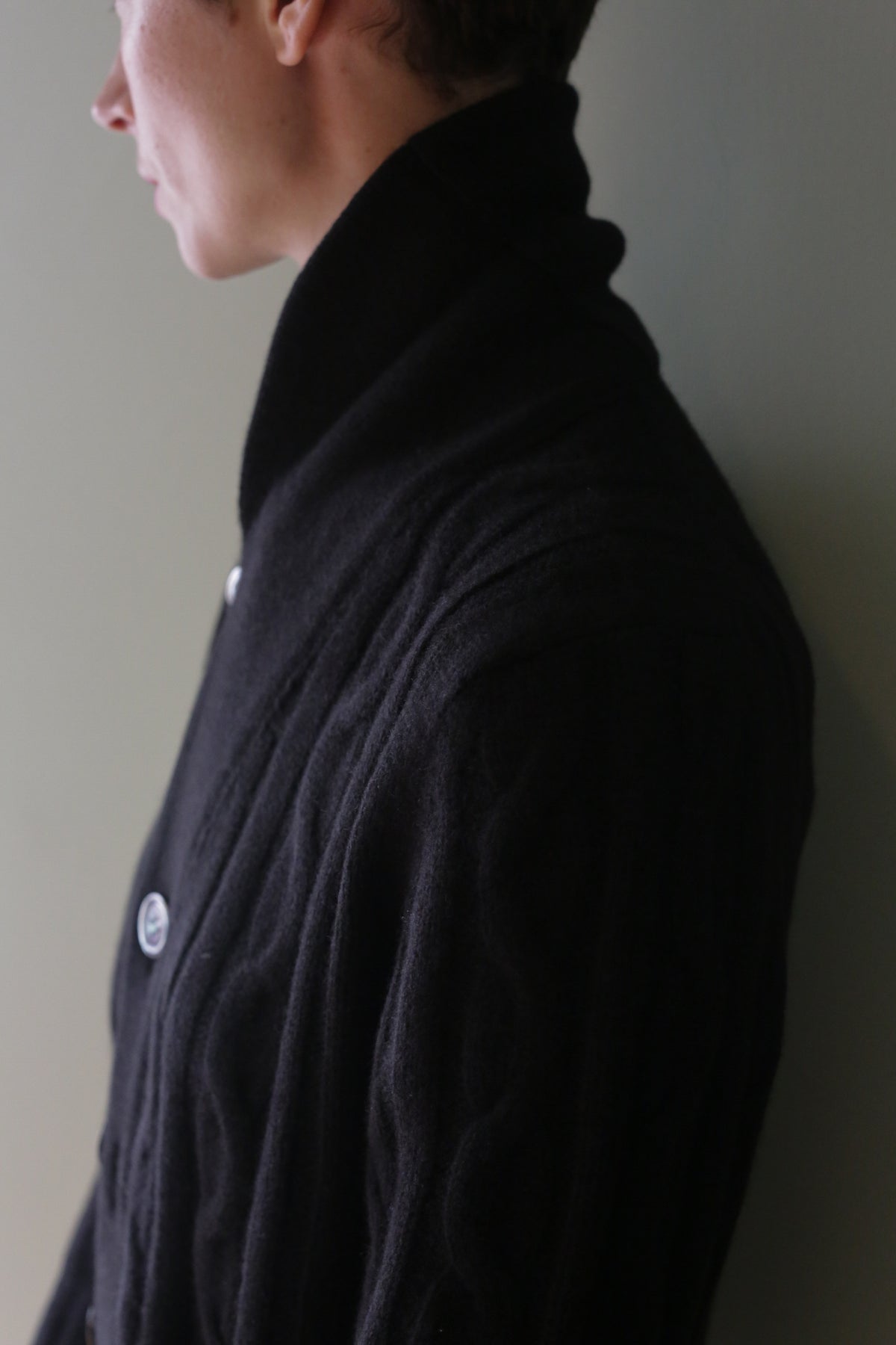 Profile view of a person wearing a black Unisex Shawl-Collar Cable-Knit Cashmere Cardigan with a wide shawl collar and visible buttons.