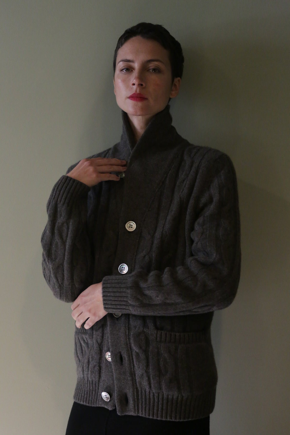 A person wearing a Unisex Shawl-Collar Cable-Knit Cashmere Cardigan in taupe, featuring a shawl collar, cable-knit texture, and large buttons.