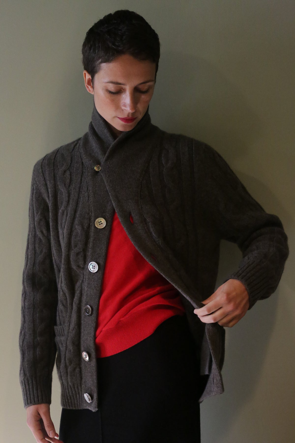 A person wearing a Unisex Shawl-Collar Cable-Knit Cashmere Cardigan | Taupe over a bright red sweater.