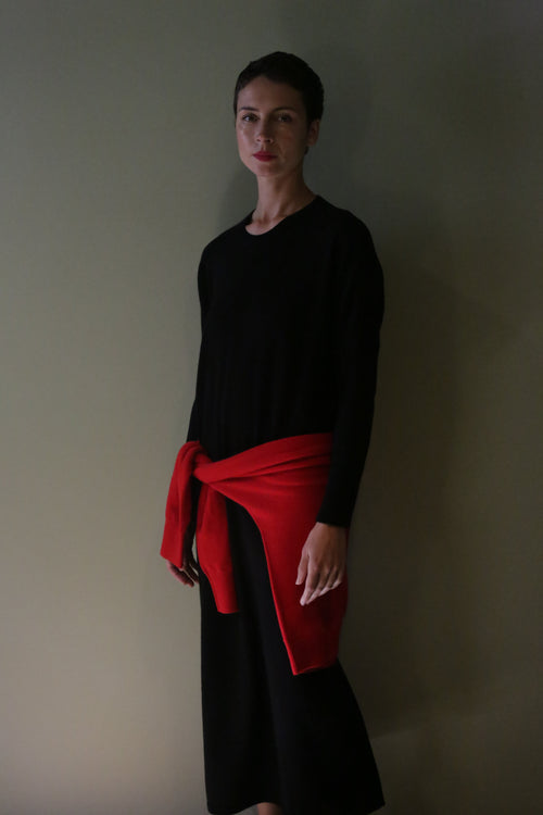 A person wearing a black Cashmere Sweater Dress in a long-sleeved midi length, with a red sweater tied around their waist.