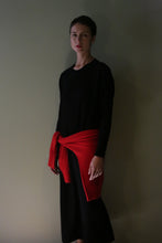 Load image into Gallery viewer, A person wearing a black Cashmere Sweater Dress in a long-sleeved midi length, with a red sweater tied around their waist.