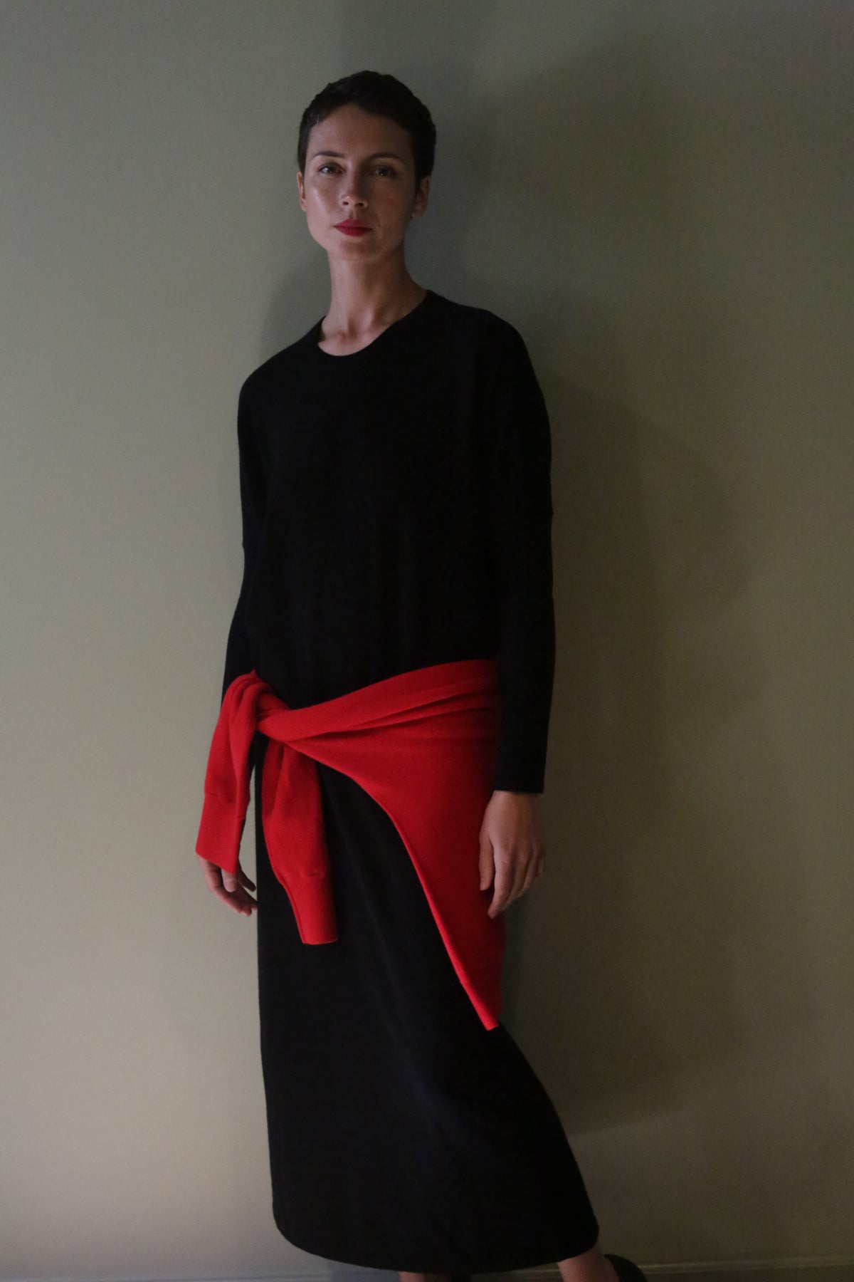 A person wearing a black Cashmere Sweater Dress in a midi length with a red sweater tied around their waist.