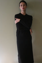 Load image into Gallery viewer, A person with short dark hair wearing a long-sleeved black sweater and a matching Cashmere Pencil Skirt | Black, standing with arms crossed.