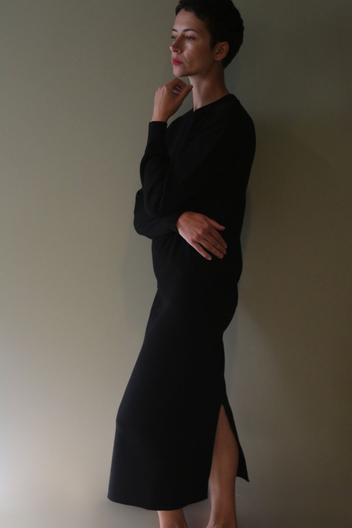 A person in a black long-sleeved sweater and a matching Cashmere Pencil Skirt | Black with a side slit.