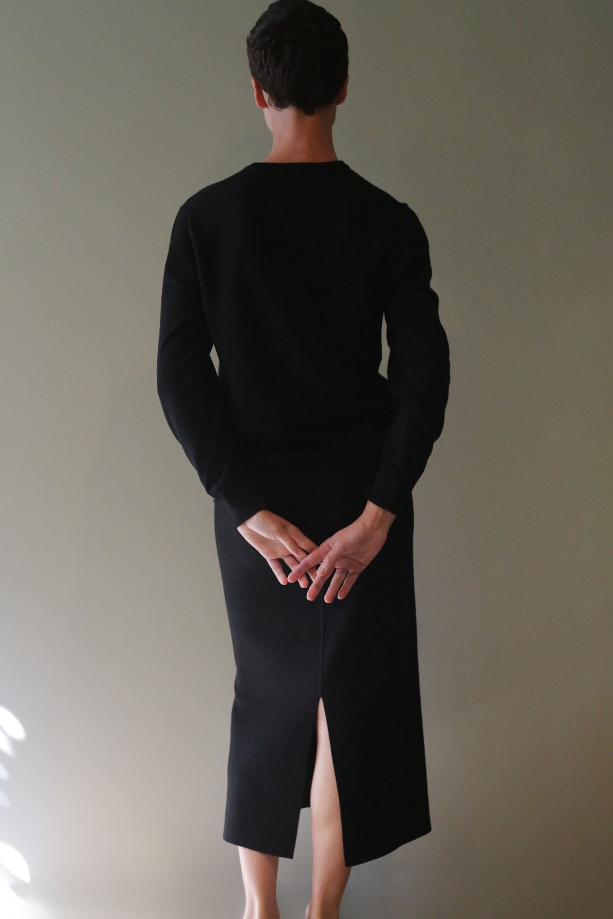A person seen from behind, wearing a black long-sleeved top and a matching Cashmere Pencil Skirt | Black with a back slit.