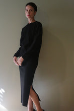 Load image into Gallery viewer, A person wearing a black long-sleeved sweater and a matching Cashmere Pencil Skirt | Black featuring a side slit.