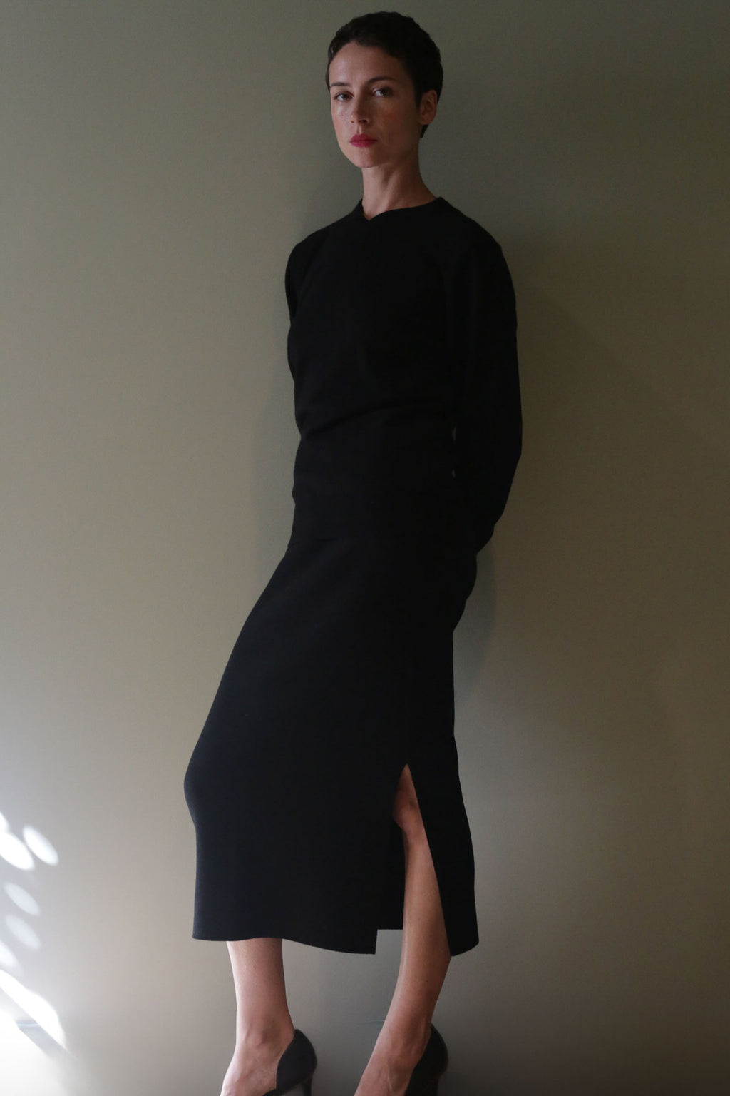 A person wearing a long-sleeved black top and a matching Cashmere Pencil Skirt | Black with a high-waisted fit and side slit.