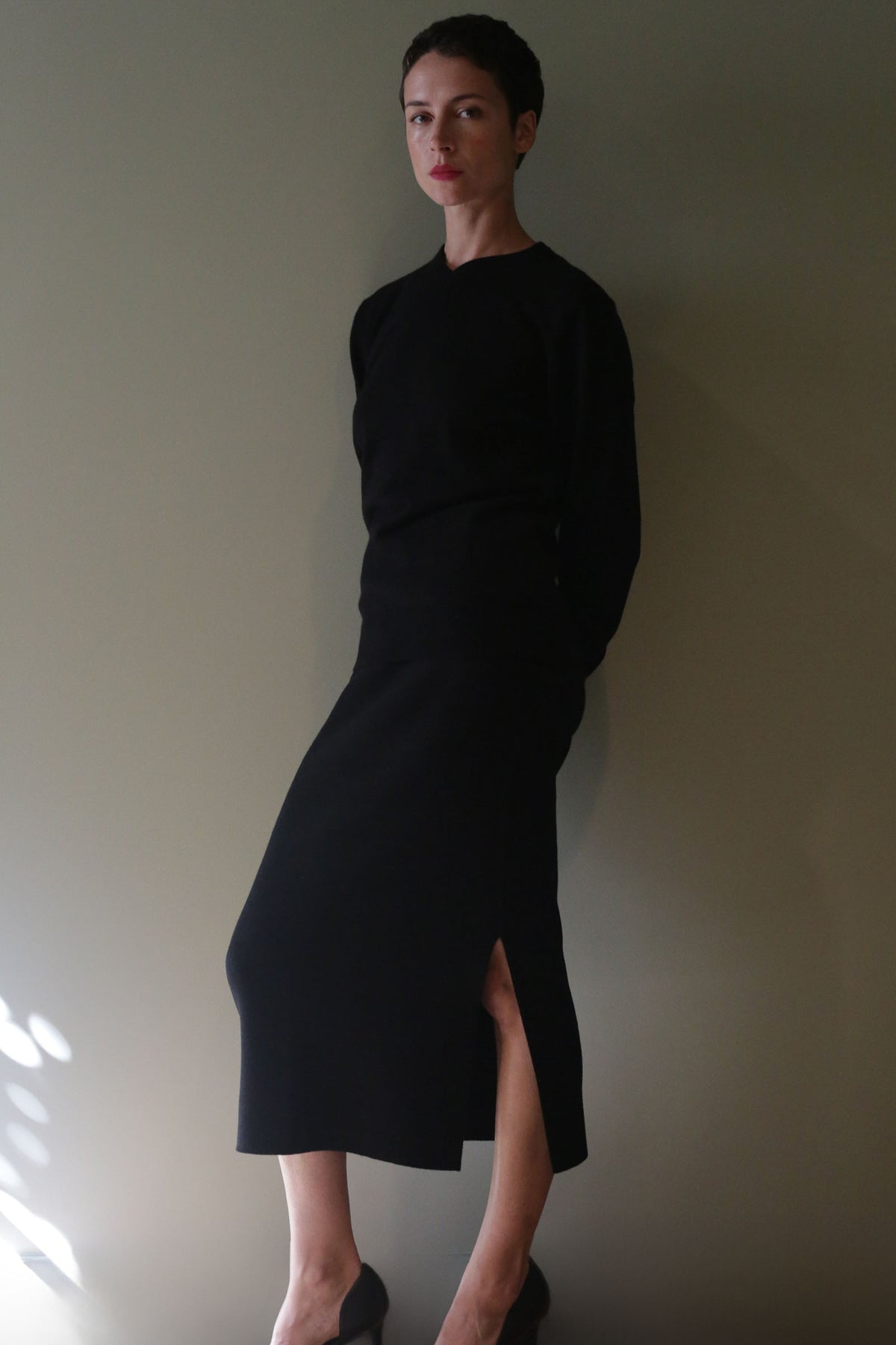 A person wearing a long-sleeved black top and a matching Cashmere Pencil Skirt | Black with a high-waisted fit and side slit.