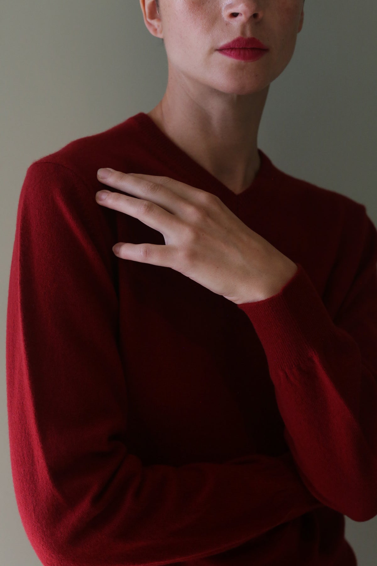 A person wearing a burgundy High V-Neck Cashmere Sweater with one hand resting on their opposite shoulder.