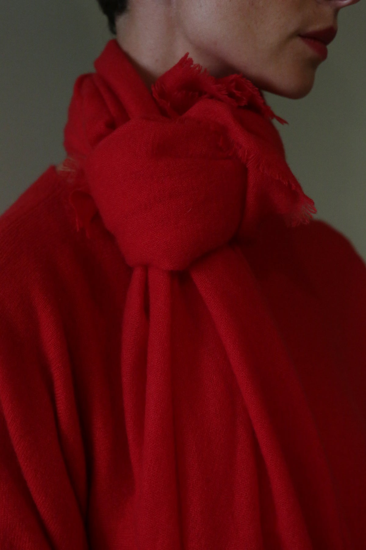 A red Tissue Weight Cashmere Scarf with frayed edges tied loosely around a person’s neck.