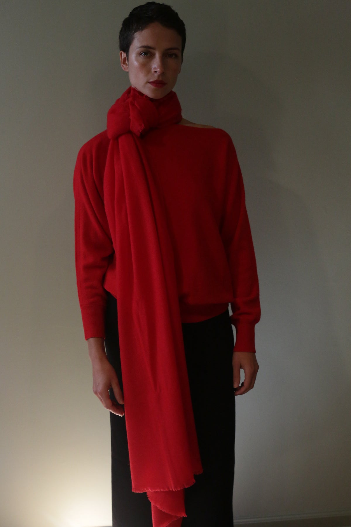 A person wearing a 36″ x 82″ Tissue Weight Cashmere Scarf in red, draped over a matching red sweater and black pants.