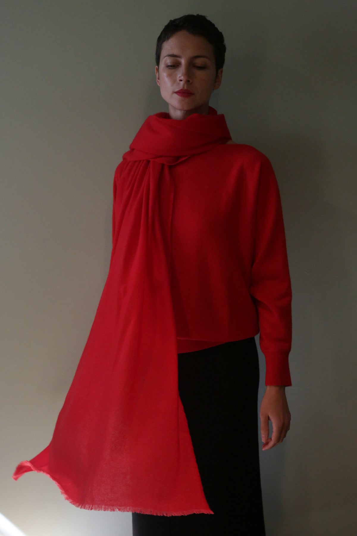A person wearing a long, red Tissue Weight Cashmere Scarf wrapped around their neck, with one end draped over their shoulder.