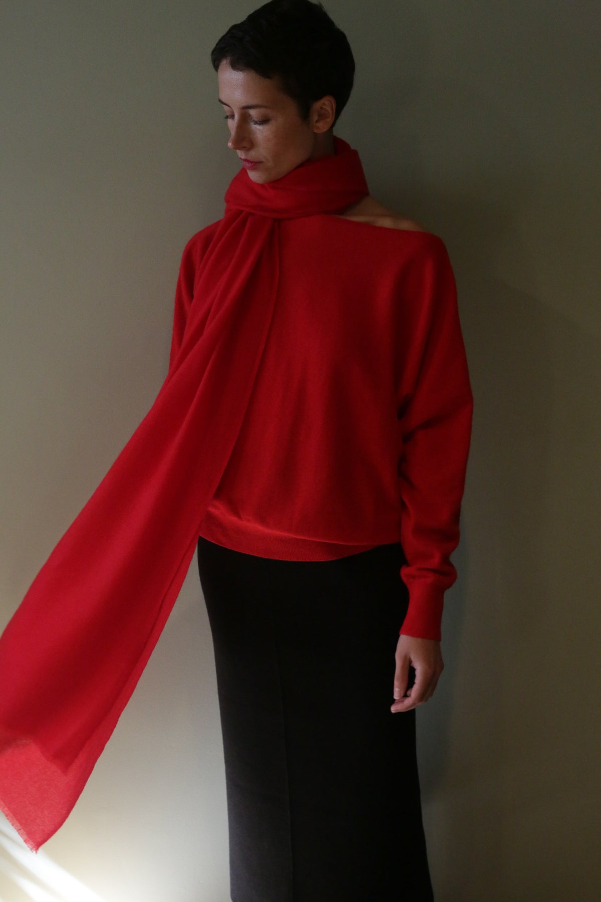 A person wearing a vermillion Tissue Weight Cashmere Scarf wrapped around their neck with one end draped over the shoulder.