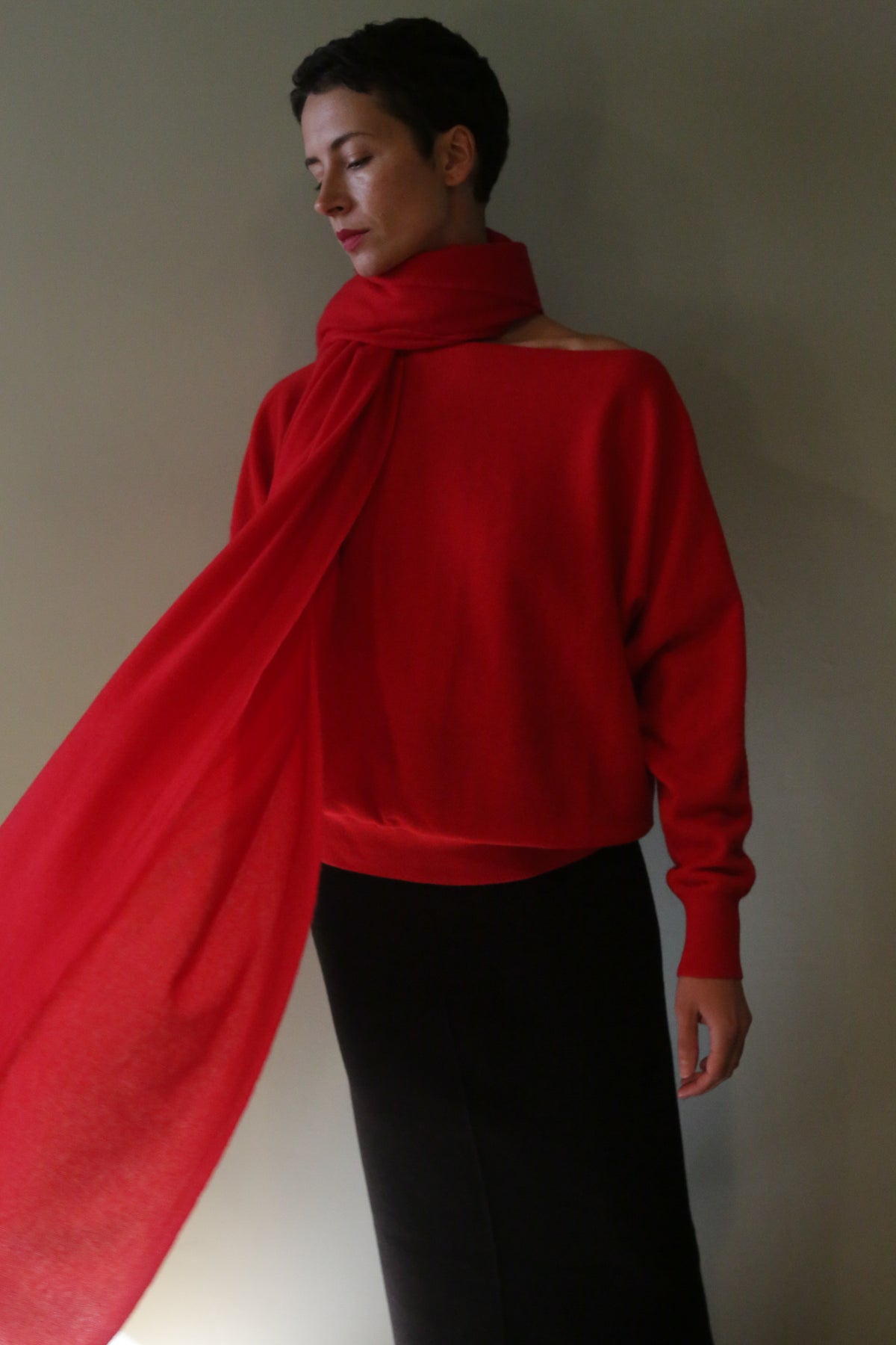 A person wearing a long, lightweight Tissue Weight Cashmere Scarf | Red draped over a matching red sweater and a black skirt.