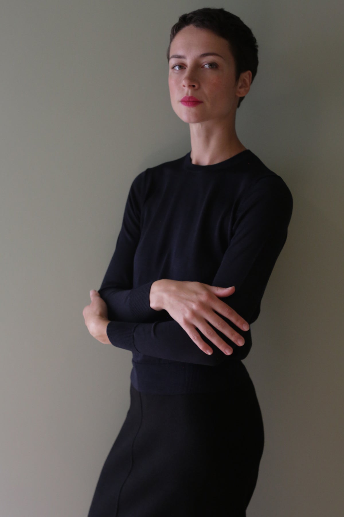 A woman with short dark hair wears a black Washable Silk Crewneck, an individually knitted, long-sleeved sweater, with her arms crossed.