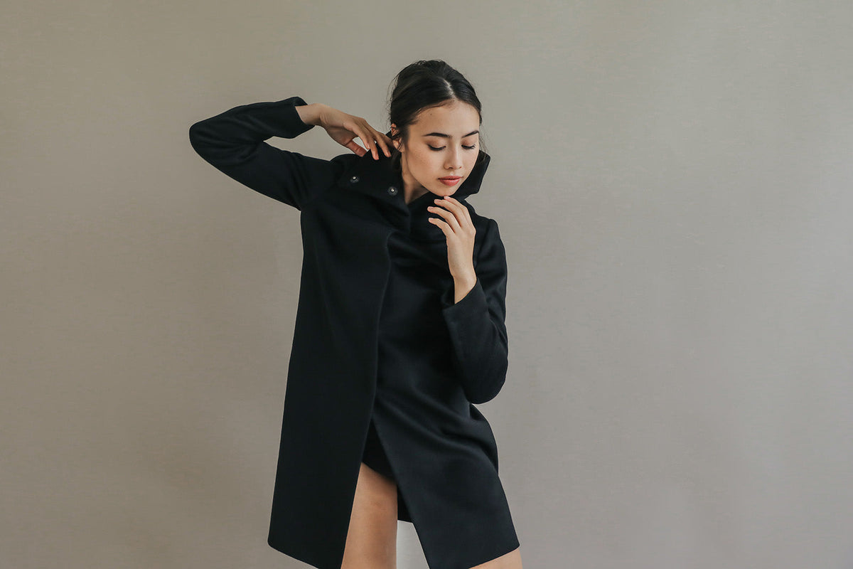 A person wearing a Stamford Long | Navy, a straight-cut, knee-length navy blue cashmere coat with a high collar.
