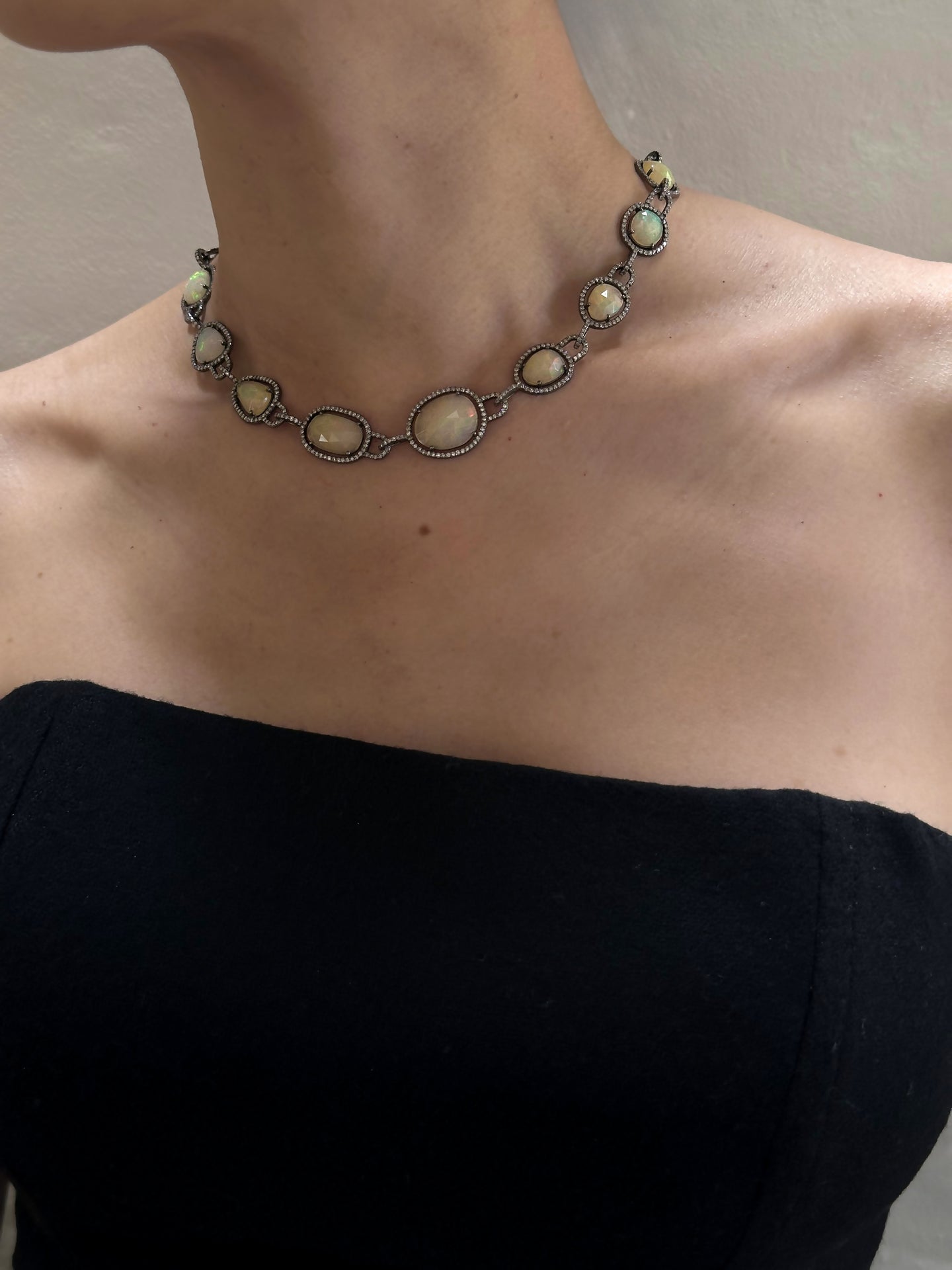 A person wearing a black strapless top and a 16” Opal Diamond Frame Necklace. The light highlights their collarbones and the intricate details of the necklace, which features interconnected oval opals.