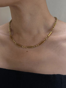 Close-up of a person's neck adorned with the "Antique 15K Gold Chain with 15K Hook and Split Ring c.1860-70," featuring a combination of rectangular and small circular links that evoke the charm of an antique English watch chain. The individual is dressed in a strapless black top against a neutral background, highlighting the necklace's minimalist and elegant design.