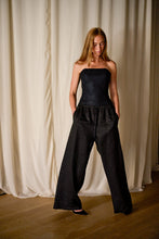 Load image into Gallery viewer, A woman with long hair stands in front of cream-colored drapes. She is wearing a strapless black top and Xiang Yun Silk Trousers, with her hands in her pockets. She looks down and has a calm expression. The room has wooden flooring.