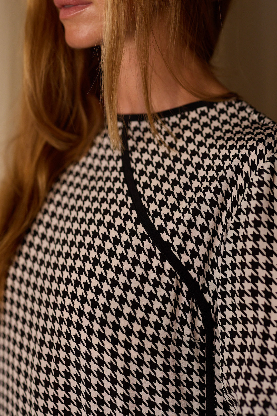 Close-up of a person with long, light brown hair wearing a Qipao Blouse | Crepe de Chine Houndstooth. The photo captures the right side of the person’s face and upper torso, highlighting the luxurious texture and intricate design of the fabric.