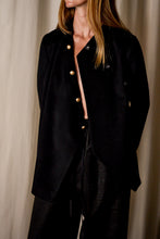 Load image into Gallery viewer, A person with long hair stands against a beige curtain background, wearing a Qipao Jacket | Cashmere Black with large gold buttons and matching black pants. They are facing slightly to the right, hands behind their back.