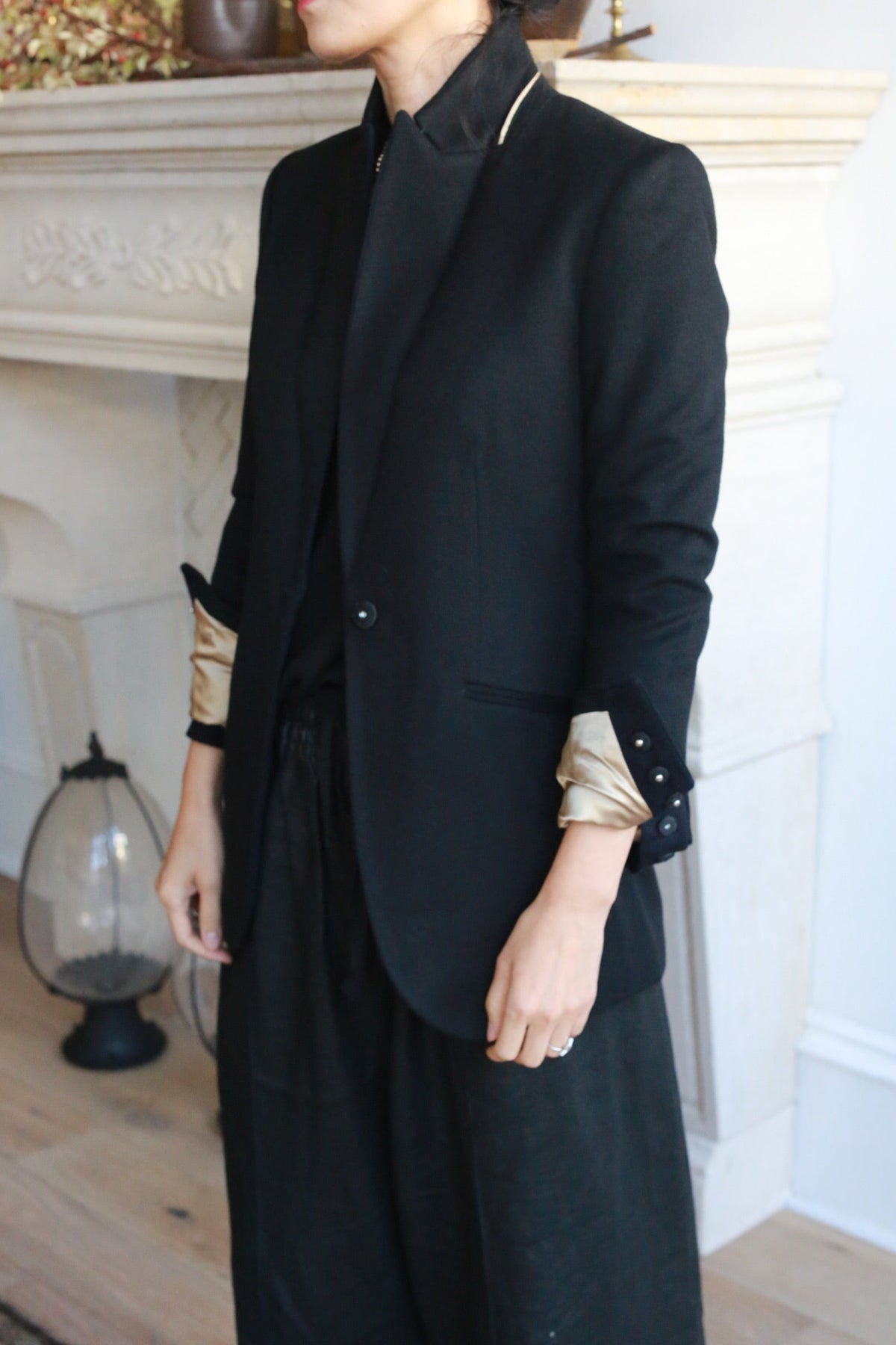 A person wearing a black Sloane | Navy / Black equestrian length tuxedo jacket with rolled sleeves revealing gold lining over a black top and trousers.
