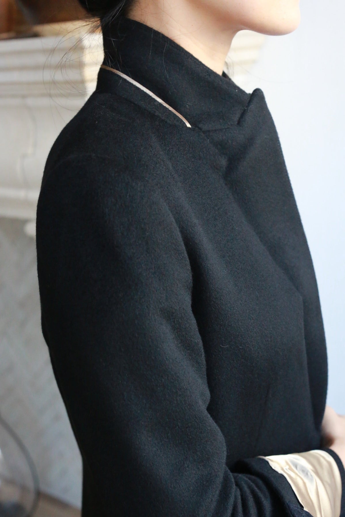 A person wearing the Sloane | Taupe / Black equestrian length black coat with a tan-colored collar detail and light-colored sleeves showing at the cuffs.
