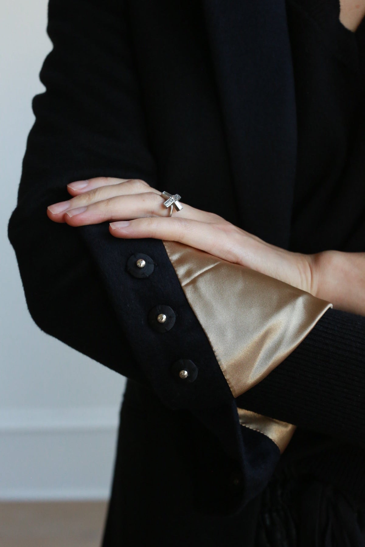 A Sloane | Taupe / Black woven cashmere tuxedo jacket with a taupe-colored sleeve lining, three decorative cuff buttons, and a silver cross ring on the hand.