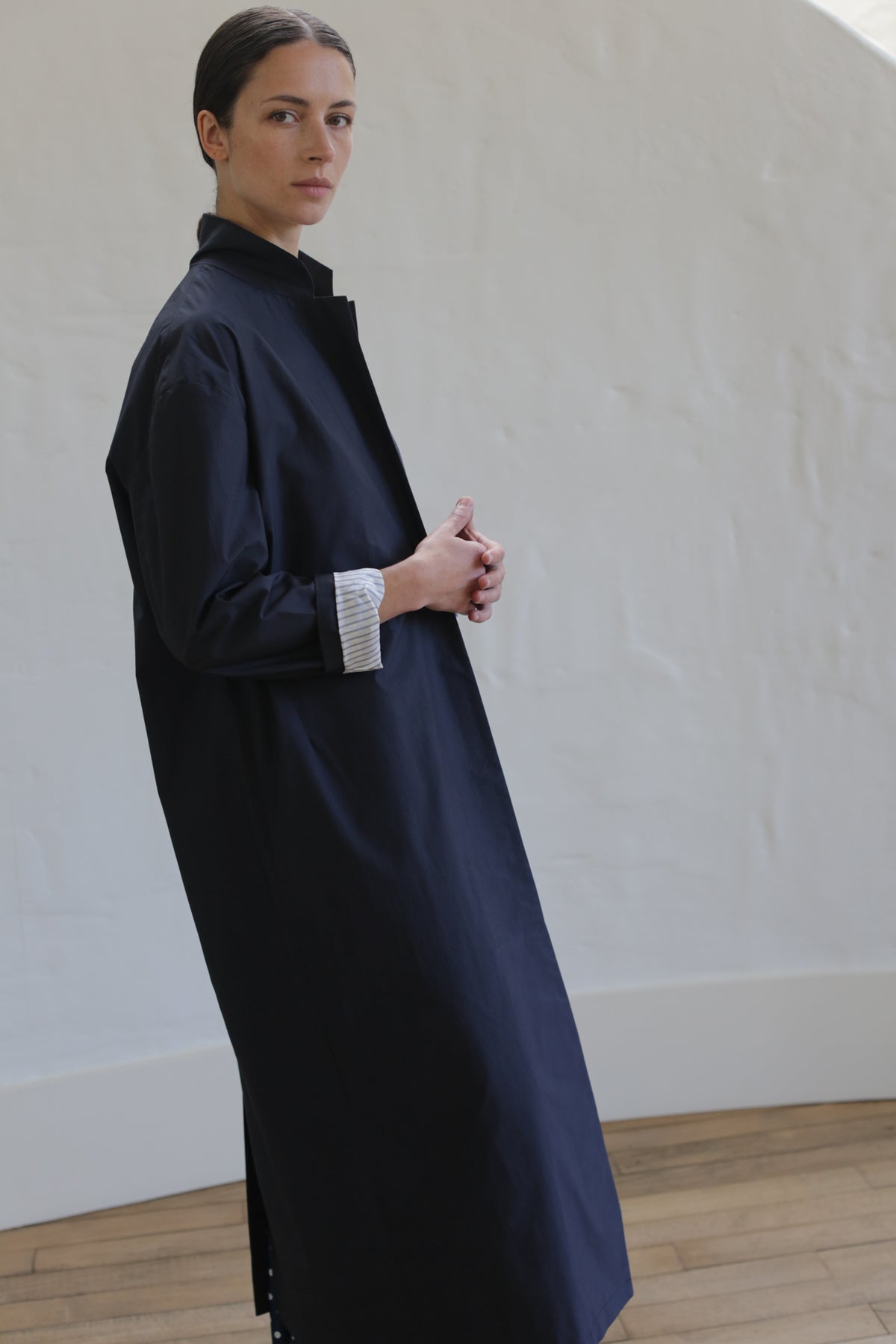 Wearing the Painter’s Coat | Navy over a white shirt, a person with dark hair pulled back stands indoors against a pale textured wall and wooden flooring.