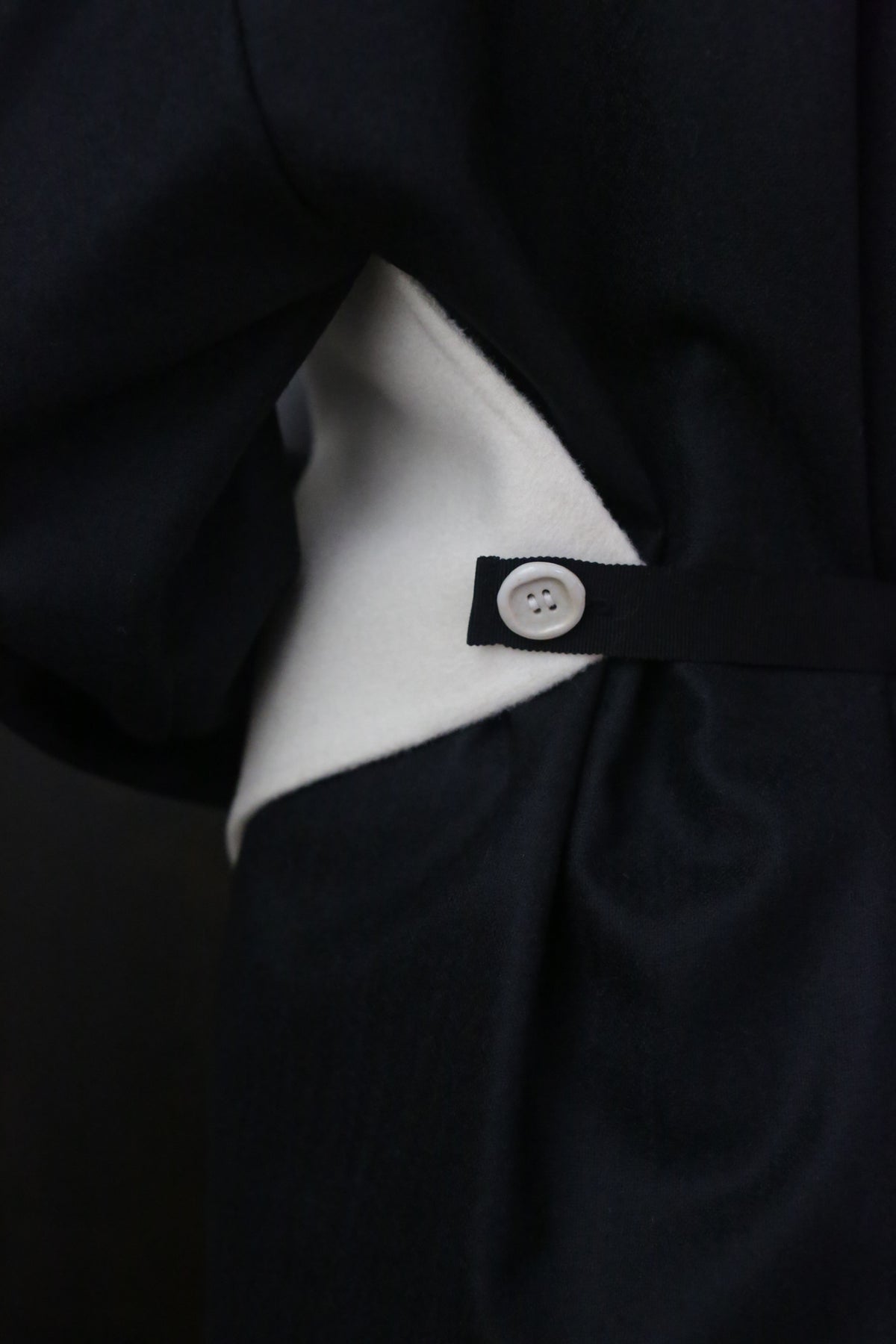 Close-up of a garment featuring black and white fabric. The image highlights a ceramic button on a black strap over the white section, contrasting with the black main material. The design suggests attention to detail and fabric interplay, utilizing zero waste design principles. This is the X Scarf - Double-face Cashmere | Undyed.