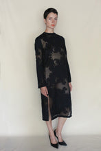 Load image into Gallery viewer, A person with short dark hair wears the Crewneck Dress | Silk Uragiri Black—long-sleeved, sheer black silk with floral patterns over beige—paired with black heels, against a plain light background. Handmade in San Francisco.